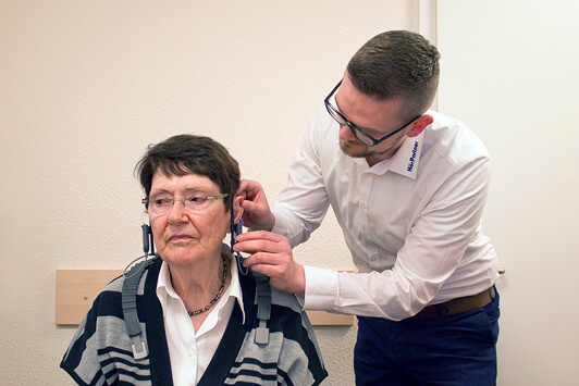 Ein Hörakustiker passt einer älteren Frau ein Hörgerät zur Hörverbesserung an.