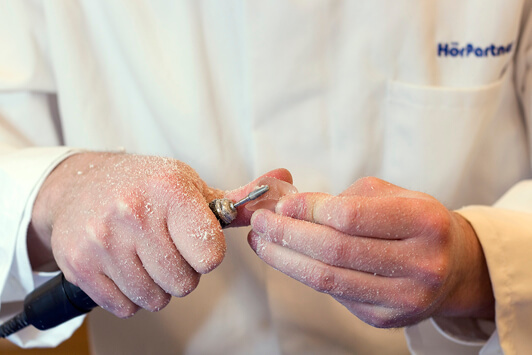 Ein Hörakustiker schleift ein Hörgerät präzise mit einem Spezialwerkzeug ab.